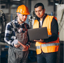Dos trabajadores de construcción e ingenieria revisando la laptop que uno de ellos sostiene en su mano.