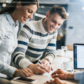 Dos personas jovenes revisando unos documentosen un escritorio mientras sonríen.