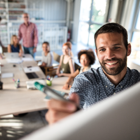 Hombre joven con un pilot frente a una pizarra, exponiendo ante un grupo de personas jovenes en una oficina.