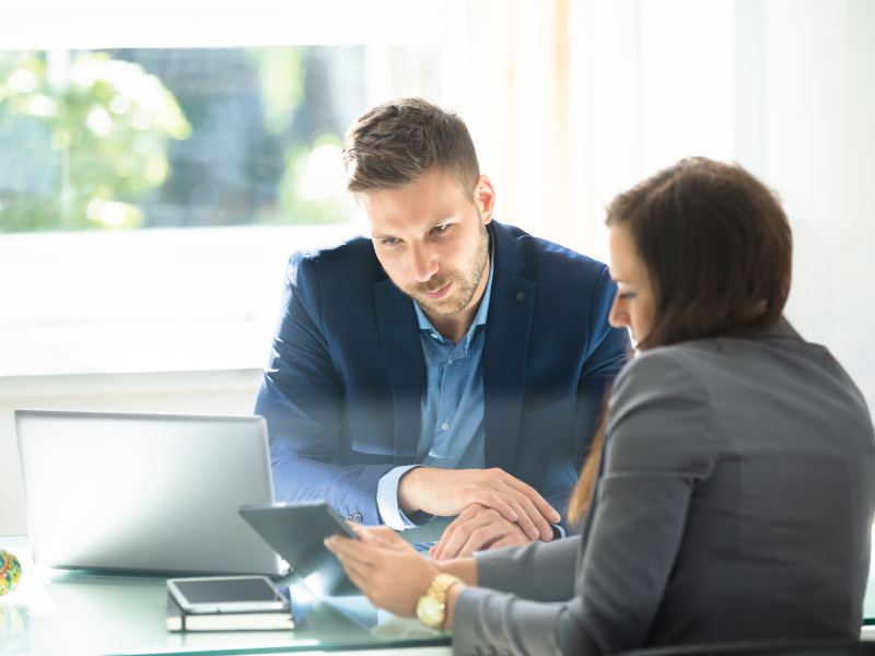 Hombre y mujer sentados en una oficina revisando su Tablet y su laptop.