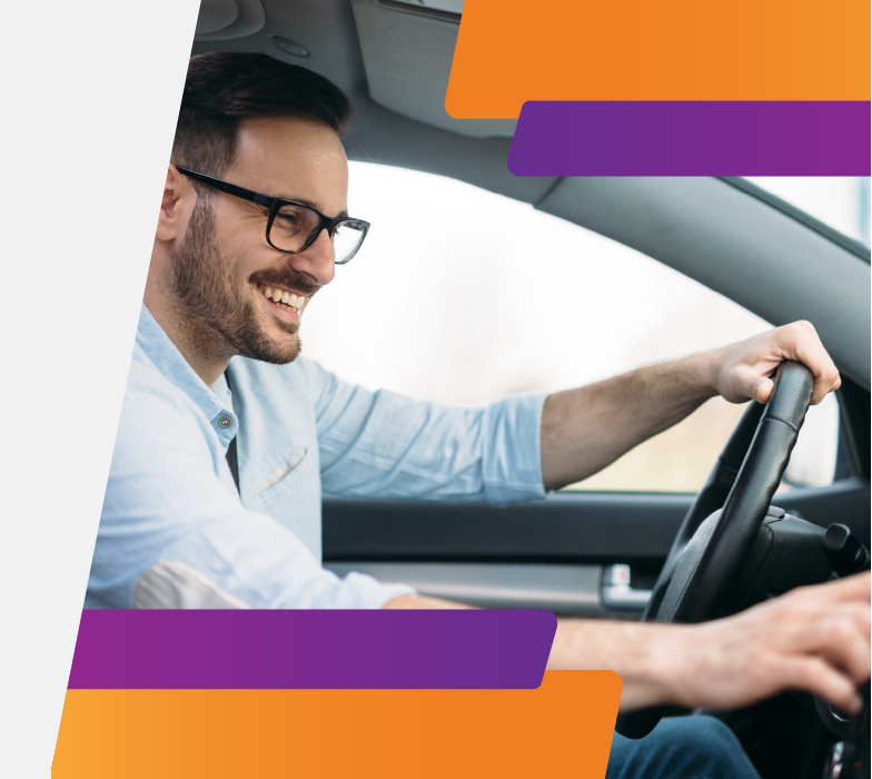 Hombre joven con lentes sonriendo al volante de su vehículo en alusión al Quick Pass de Tarjeta de Crédito.