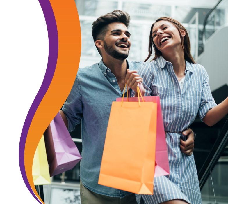 Pareja joven sonriendo mientras caminan en centro comercial cargando bolsas de compras.