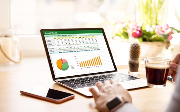 Una computadora sobre una mesa, que muestra la herramienta de excel abierta con varios gráficos.