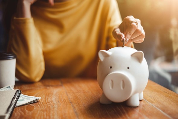 Persona echando una moneda sobre un chanchito de cerámica, que está sobre una mesa.