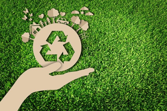 Figura de Mano de cartón mostrando el símbolo de reciclaje y sus beneficios sobre fondo verde de zacate.