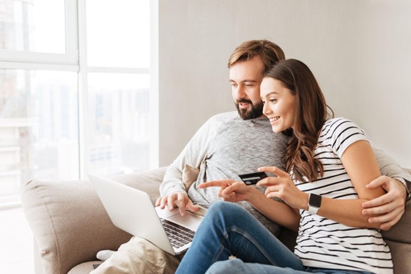 Pareja sentada en un sillón con una tarjeta en mano y revisando computadora
