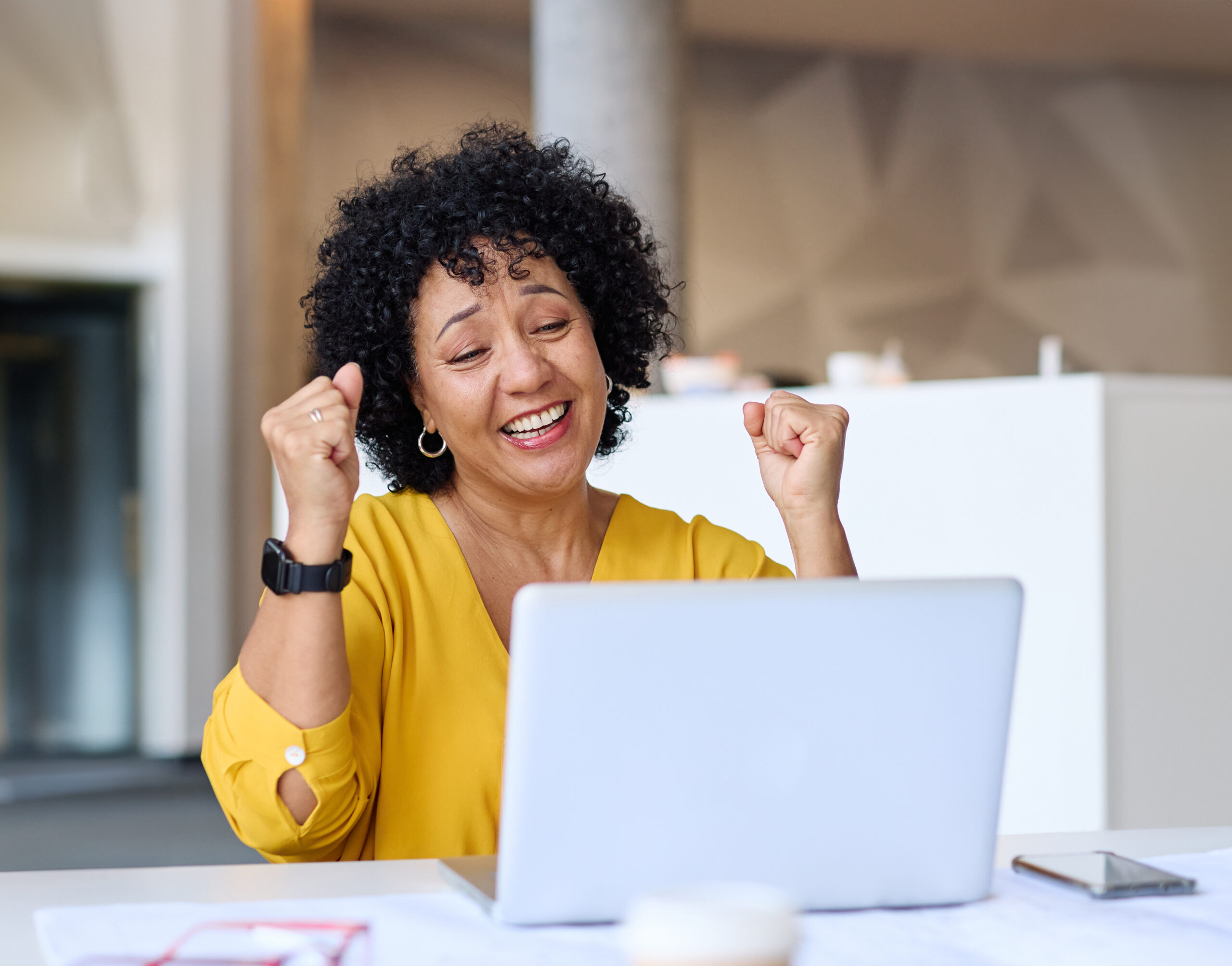 Mujer con cabello rizado, sonriendo y celebrando frente a su laptop.