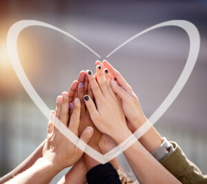 Varias manos de diferentes personas unidas en alto, formando un gesto de unión y solidaridad, con un corazón dibujado alrededor.