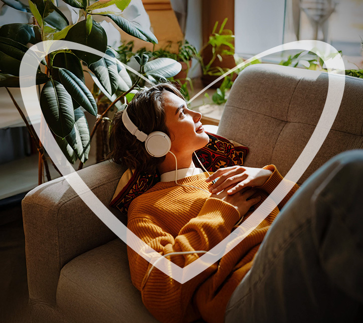 Persona recostada en el sofá escuchando música con audífonos, rodeada por un corazón transparente