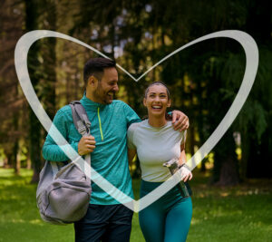 Pareja sonriente caminando por un parque con ropa deportiva, rodeados por un corazón transparente.