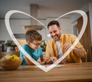 Padre e hijo jugando y riendo juntos en la mesa de la cocina, rodeados por un corazón transparente