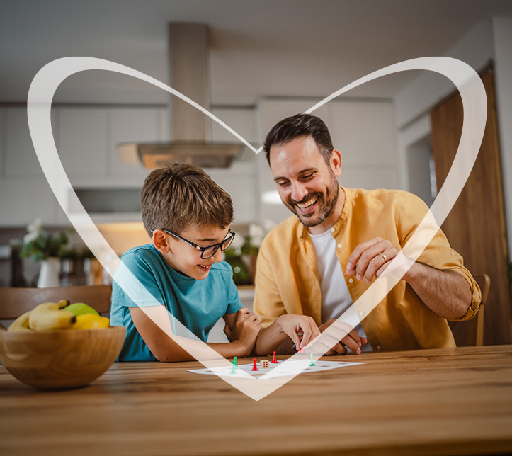 Padre e hijo jugando y riendo juntos en la mesa de la cocina, rodeados por un corazón transparente