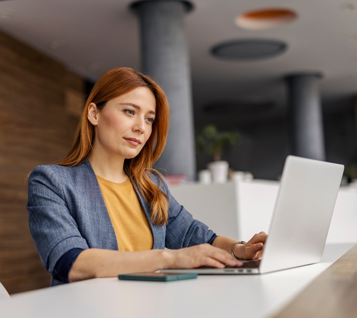 Portrait of smart casual female executive sitting at corporate office and typing on a laptop.