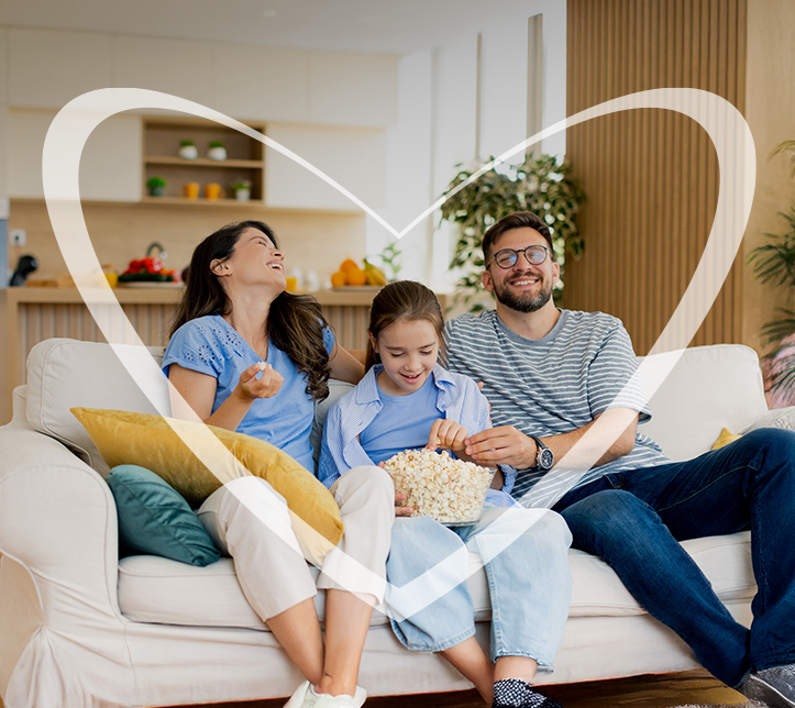 Familia sentada en el sillón de la sala mientras comen palomitas, compartiendo tiempo de Calidad en Familia.