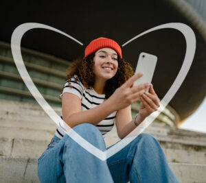Mujer joven sonriendo, sentada en unas gradas mientras mira su celular para iniciar un ahorro.