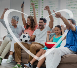 Imagen de una familia de diferentes generaciones reunida en la sala de su hogar disfrutando de un partido de fútbol. Todos muestran expresiones de alegría y celebración, transmitiendo emociones asociadas con la unión familiar, el entretenimiento y la pasión por el deporte