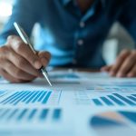 Person reviews financial charts with a pen, highlighting insights in a bright office, perfect for business or financial planning materials.