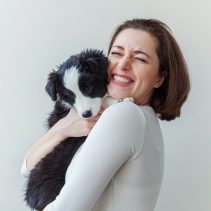 Smiling young attractive woman embracing cute puppy dog border collie isolated on white background. Girl huging new lovely member of family. Pet care and animals concept