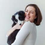 Smiling young attractive woman embracing cute puppy dog border collie isolated on white background. Girl huging new lovely member of family. Pet care and animals concept