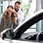 Picture of adult man making surprise to beautiful woman in car showroom