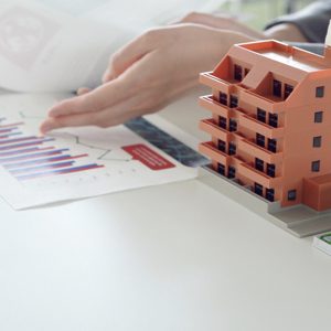 imagen de dos personas y una de ellas esta señalando una hoja con un gráfico. Tambien hay dos edificios en miniatura y